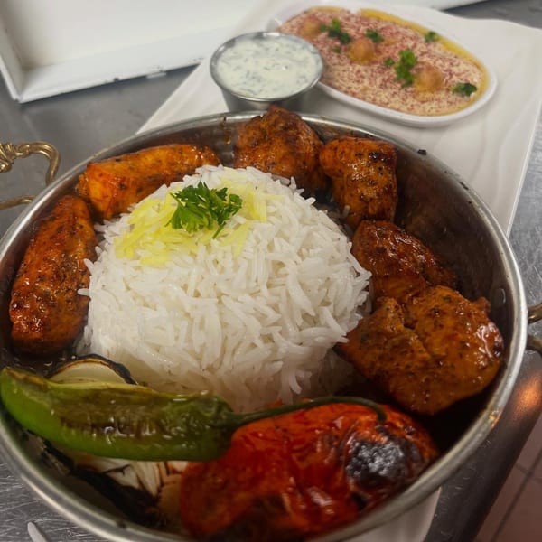 Middle-Eastern chicken kebab with rice, grilled vegetables, and a side of hummus and yogurt sauce.