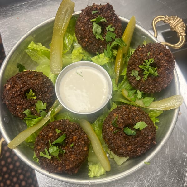 Middle-eastern falafel with lettuce, pickles, and a side of white sauce in a metal bowl.