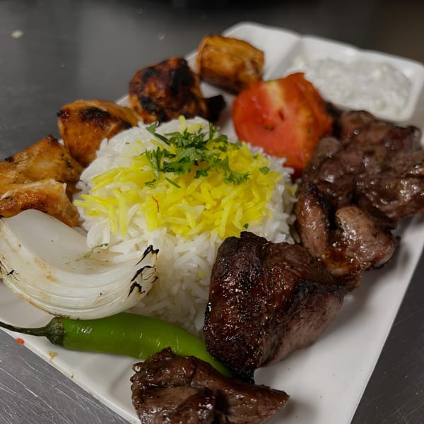 A middle-eastern platter with grilled chicken and beef, rice, grilled onion, tomato, and a green chili.