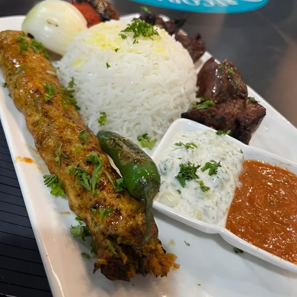Middle-Eastern platter with kofta kebab, rice, grilled vegetables, and two dipping sauces.
