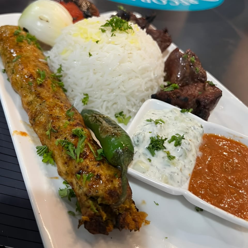 Middle-Eastern platter with kofta kebab, rice, grilled vegetables, and two dipping sauces.