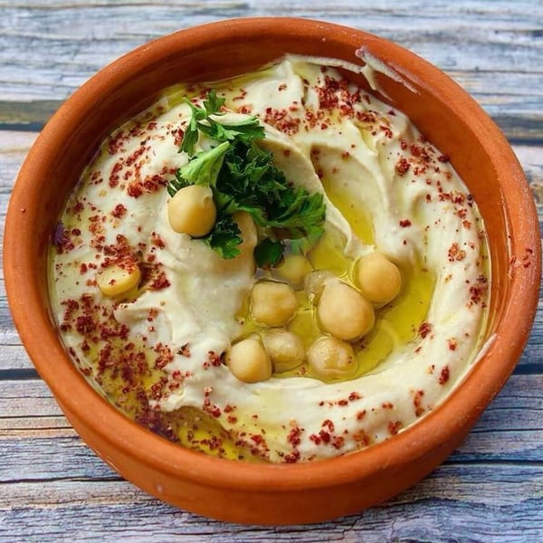 Creamy hummus in a terracotta bowl, garnished with chickpeas, olive oil, sumac, and parsley.