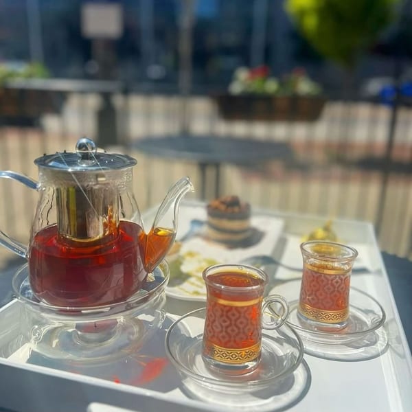 Middle-Eastern tea set with a glass teapot and two ornate tea glasses on a white tray outdoors.