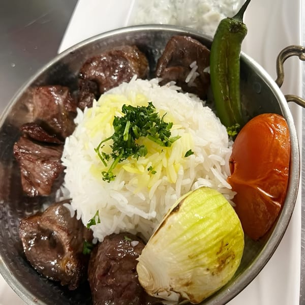 Middle-eastern dish with beef chunks, white and yellow rice, grilled tomato, onion, and green pepper.